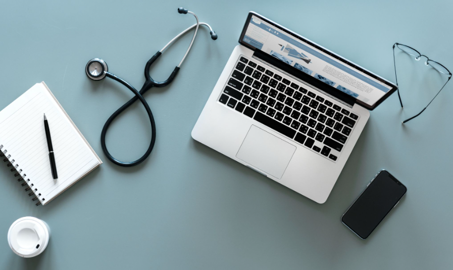 Mesa com notebook, estetoscópio e celular representando marketing digital para clínicas e presença médica online.