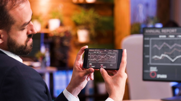 Executivo analisando indicadores de desempenho em smartphone e monitor, representando estratégia de conteúdo, SEO, AEO e GEO para empresas B2B na nova era do Google.